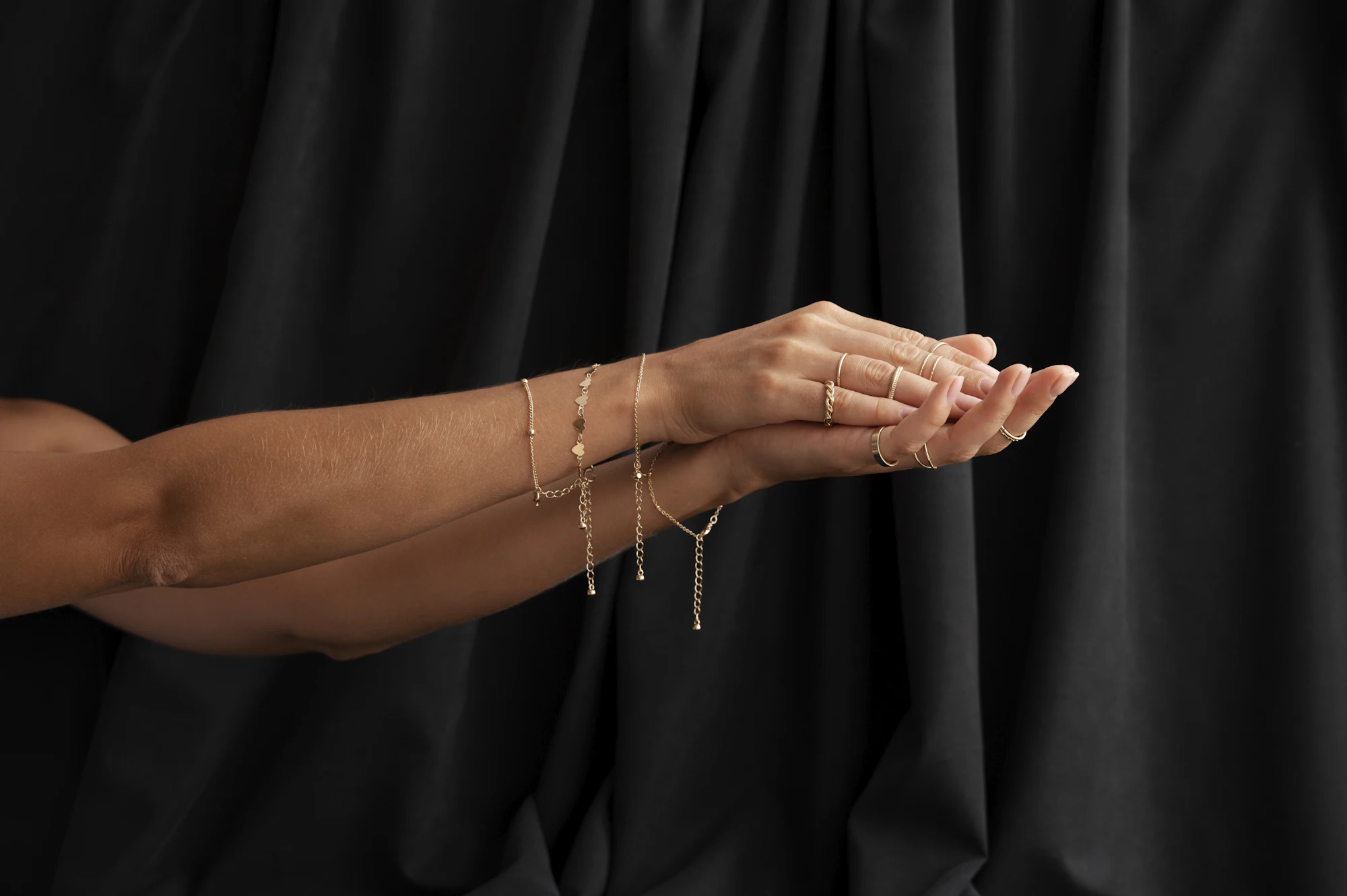 Mãos com pulseiras e anéis dourados sobre um tecido preto